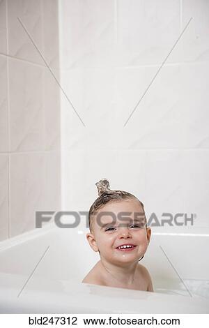 Stock Image - Smiling Caucasian girl in bubble bath. Fotosearch