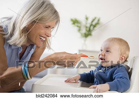 Smiling Caucasian grandmother feeding baby grandson in high chair View Large Photo Image Picture - Smiling Caucasian grandmother feeding baby grandson in high chair. Fotosearch