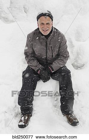 Stock Photo - Smiling Caucasian man sitting on pile of snow. Fotosearch