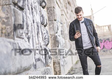 Stock Image - Smiling Caucasian man walking on sidewalk texting on cell phone. Fotosearch