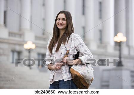 Stock Image - Smiling Caucasian woman carrying backpack at school. Fotosearch