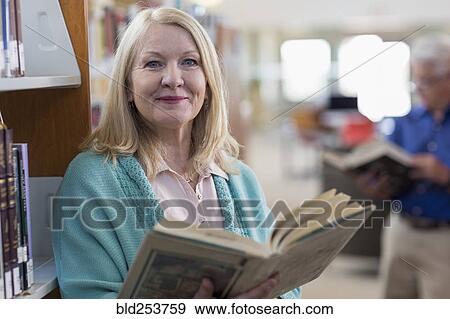 Stock Photo - Smiling Caucasian woman holding book in library. Fotosearch