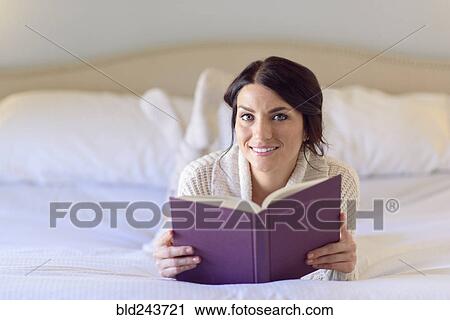Smiling Caucasian woman laying on bed reading book View Large Photo Image Stock Image - Smiling Caucasian woman laying on bed reading book. Fotosearch