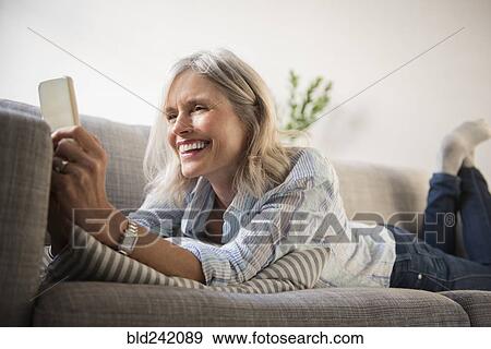 Smiling Caucasian woman laying on sofa texting on cell phone View Large Photo Image Stock Photo - Smiling Caucasian woman laying on sofa texting on cell phone. Fotosearch