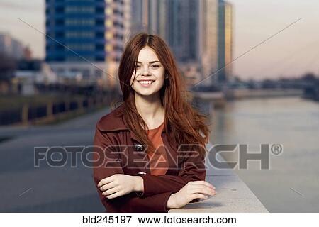 Stock Photo - Smiling Caucasian woman leaning on wall at waterfront. Fotosearch