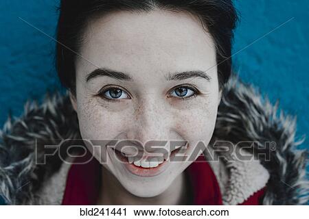 Stock Image - Smiling Caucasian woman near blue wall. Fotosearch