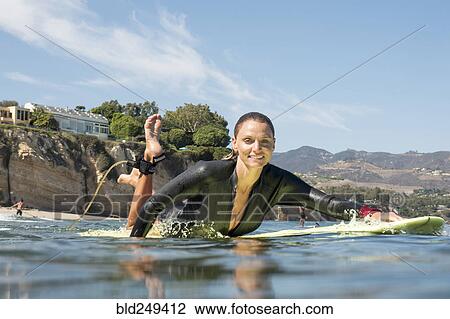 Stock Image - Smiling Caucasian woman paddling on surfboard in ocean. Fotosearch