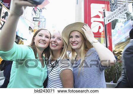 Stock Image - Smiling Caucasian woman posing for cell phone selfie in city. Fotosearch