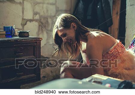 Stock Image - Smiling Caucasian woman sitting on bed looking down. Fotosearch