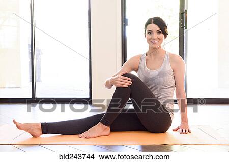 Picture - Smiling Caucasian woman sitting on exercise mat. Fotosearch