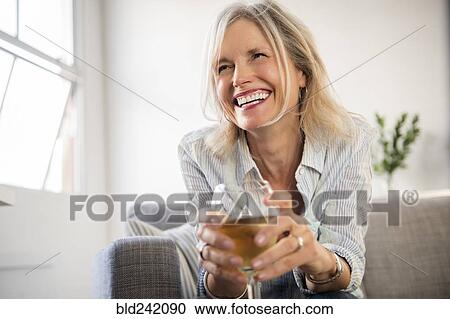 Smiling Caucasian woman sitting on sofa drinking white wine View Large Photo Image Stock Image - Smiling Caucasian woman sitting on sofa drinking white wine. Fotosearch