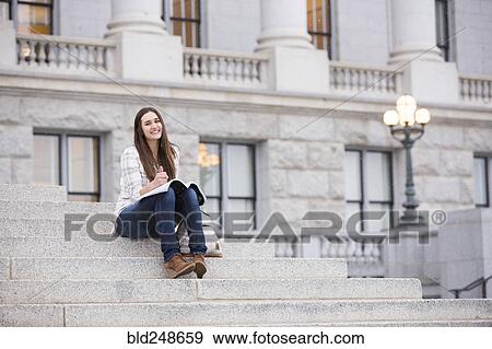 Stock Photo - Smiling Caucasian woman sitting on staircase holding notebook. Fotosearch