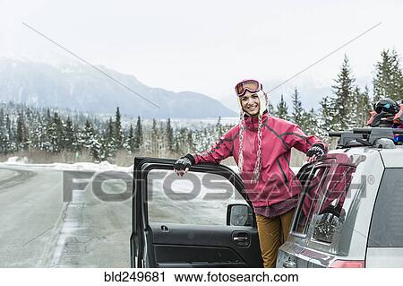 Stock Image - Smiling Caucasian woman standing in car in winter. Fotosearch