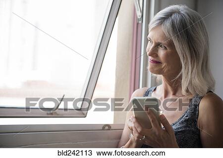 Smiling Caucasian woman texting on cell phone near window View Large Photo Image Stock Image - Smiling Caucasian woman texting on cell phone near window. Fotosearch