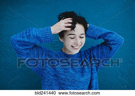 Smiling Caucasian woman tousling hair near blue wall View Large Photo Image Stock Image - Smiling Caucasian woman tousling hair near blue wall. Fotosearch