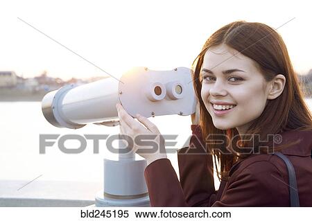 Stock Photography - Smiling Caucasian woman using binoculars at waterfront. Fotosearch