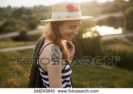 Stock Photography - Smiling Caucasian woman wearing sun hat carrying sweater. Fotosearch