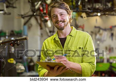Picture - Smiling Caucasian worker writing on clipboard in bicycle shop. Fotosearch
