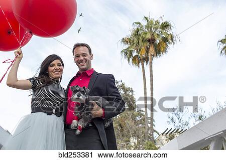 Smiling couple holding dog and red balloons View Large Photo Image Stock Image - Smiling couple holding dog and red balloons. Fotosearch