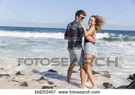 Stock Photo - Smiling couple hugging on windy beach. Fotosearch