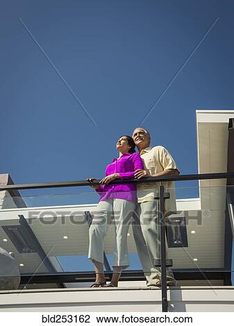 Stock Image - Smiling couple standing on modern balcony. Fotosearch