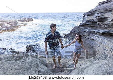 Stock Photo - Smiling couple walking on rock formations at beach. Fotosearch