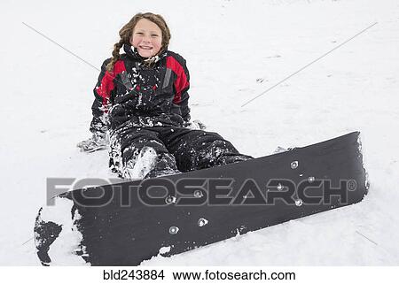Picture - Smiling girl sitting in snow with snowboard. Fotosearch