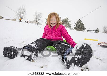 Stock Image - Smiling girl sitting on toboggan in snow. Fotosearch