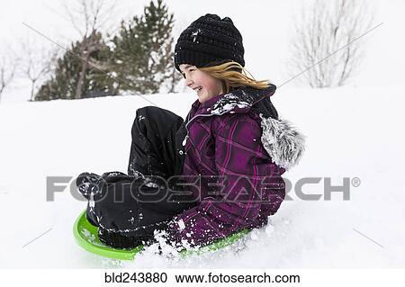 Stock Image - Smiling girl sliding on toboggan in snow. Fotosearch