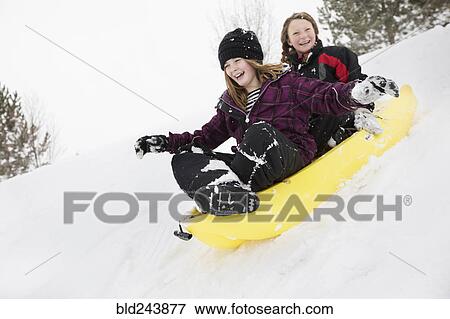 Smiling girls sliding in toboggan on hill in winter View Large Photo Image Stock Photo - Smiling girls sliding in toboggan on hill in winter. Fotosearch