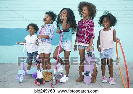 Stock Image - Smiling girls standing on sidewalk with transportation. Fotosearch