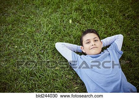 Stock Image - Smiling Hispanic boy laying in grass. Fotosearch