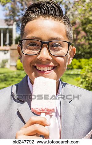 Stock Image - Smiling Hispanic boy wearing suit eating popsicle. Fotosearch