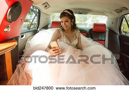 Stock Image - Smiling Hispanic girl texting on cell phone in limousine. Fotosearch
