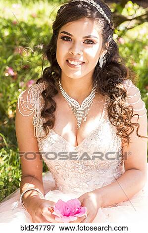 Stock Photo - Smiling Hispanic girl wearing gown holding flower. Fotosearch