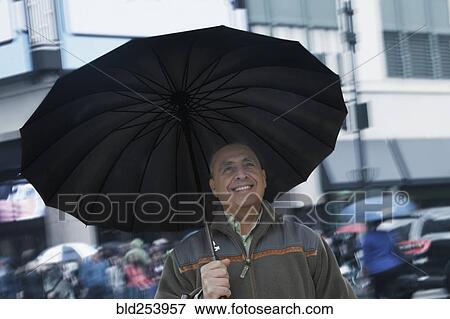 Smiling Hispanic man holding umbrella in city View Large Photo Image Stock Photo - Smiling Hispanic man holding umbrella in city. Fotosearch