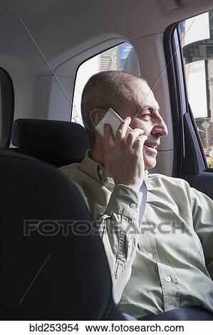 Picture - Smiling Hispanic man riding in car and talking on cell phone. Fotosearch