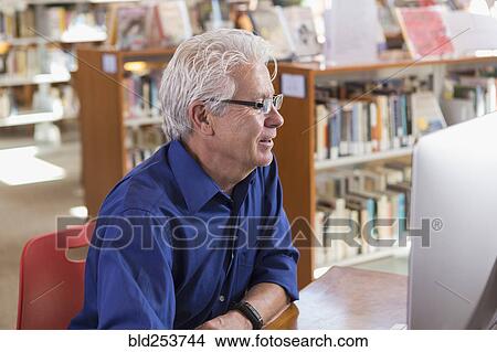 Picture - Smiling Hispanic man using computer in library. Fotosearch