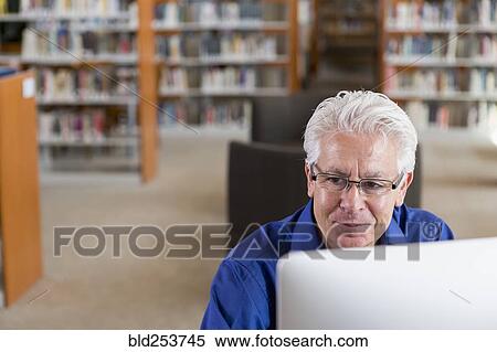 Stock Photography - Smiling Hispanic man using computer in library. Fotosearch