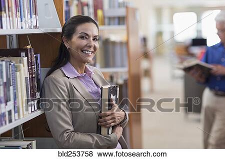Stock Photo - Smiling Hispanic woman holding book in library. Fotosearch