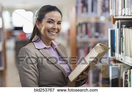Smiling Hispanic woman holding book in library View Large Photo Image Stock Photo - Smiling Hispanic woman holding book in library. Fotosearch