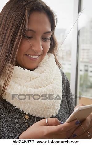 Stock Photo - Smiling Hispanic woman texting on cell phone. Fotosearch