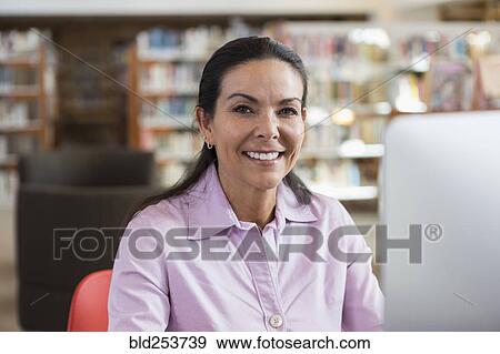 Stock Photo - Smiling Hispanic woman using computer in library. Fotosearch