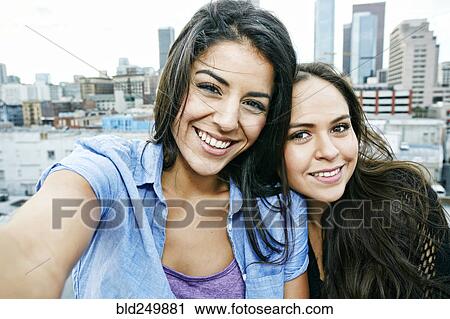 Stock Image - Smiling Hispanic women posing on urban rooftop. Fotosearch