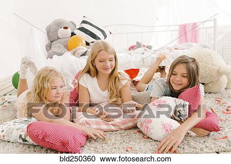 Stock Image - Smiling Middle Eastern girls laying on floor watching bubbles. Fotosearch