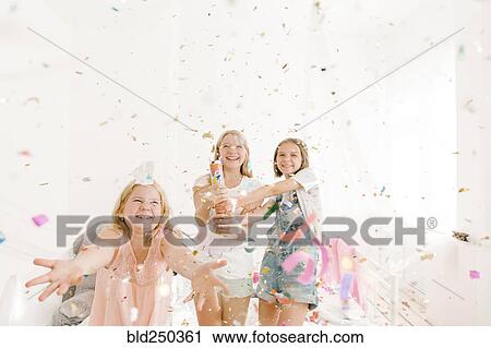 Stock Image - Smiling Middle Eastern girls throwing confetti in bedroom. Fotosearch