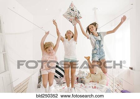Stock Image - Smiling Middle Eastern sisters jumping off bed. Fotosearch