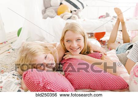 Stock Photograph - Smiling Middle Eastern sisters laying on floor. Fotosearch