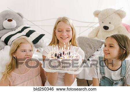 Stock Photograph - Smiling Middle Eastern sisters with birthday cake in bedroom. Fotosearch