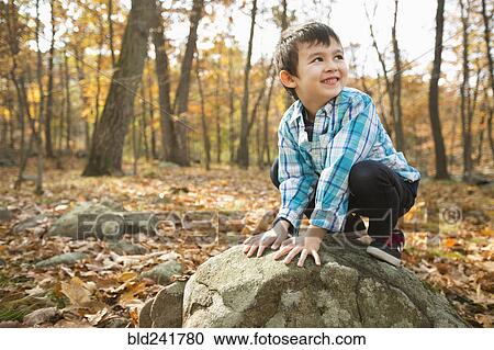 Stock Image - Smiling Mixed Race boy crouching on rock in autumn. Fotosearch